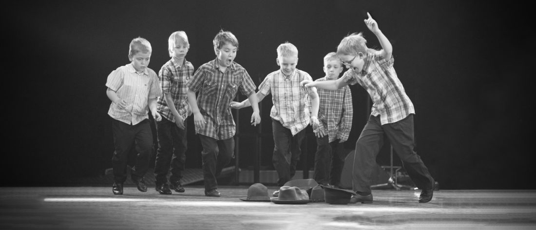 Kuusi poikaa säntää kohti teatterilavalla lepääviä hattuja.